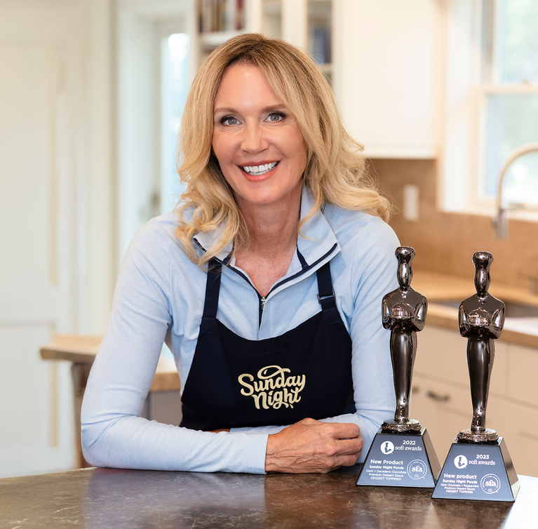 Founder Eileen Gannon poses in her kitchen with her Sunday Night apron and two Sofi Awards.