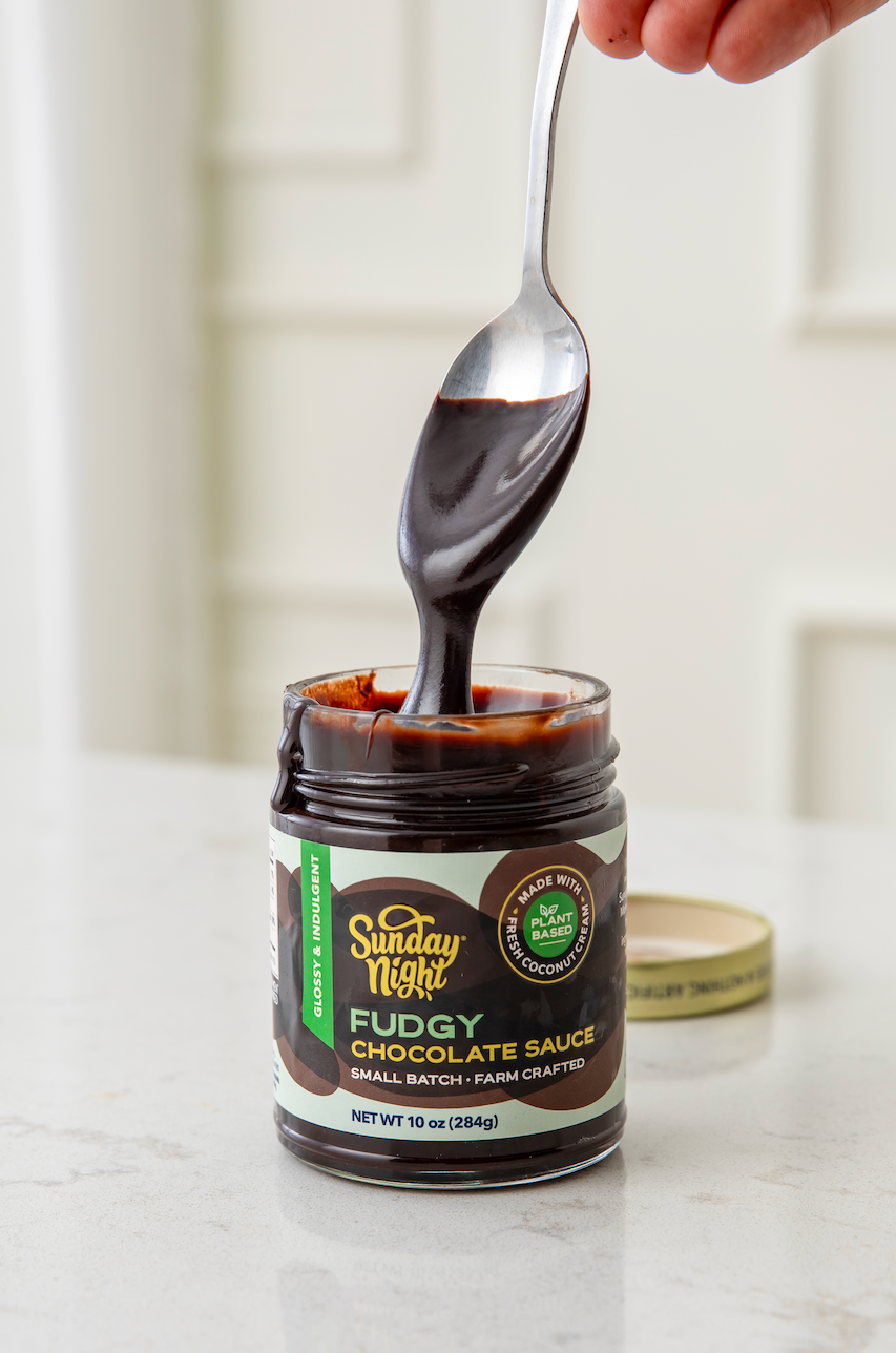A spoon is  pulling up from dipping into the Sunday Night's Vegan Fudgy Chocolate Sauce.