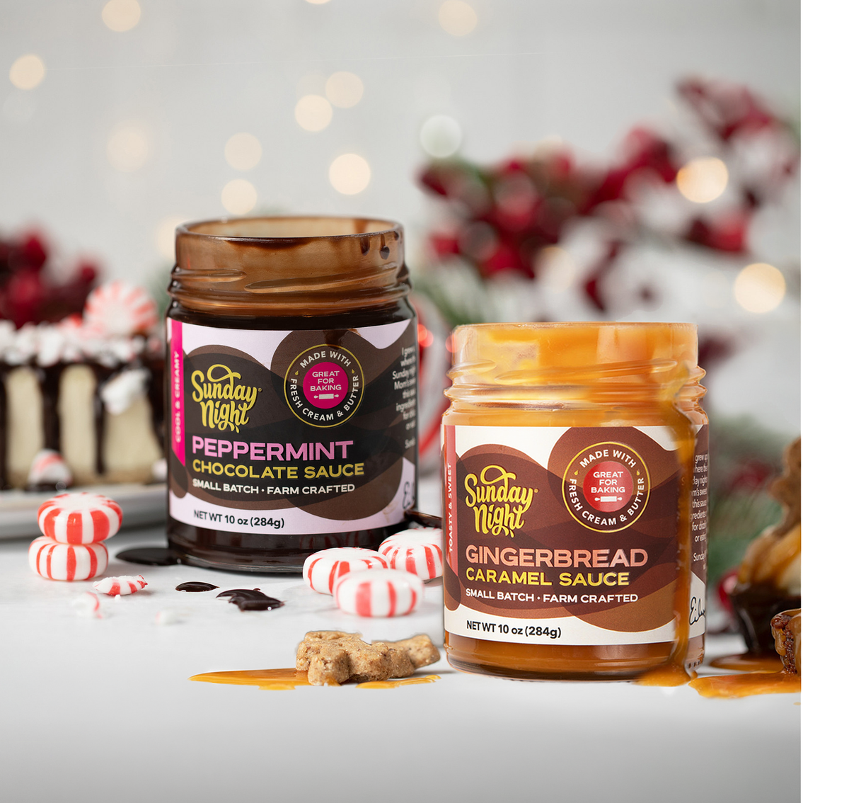 Holiday lights and greenery offset the colorful and open jars of gingerbread caramel sauce and peppermint chocolate sauce. A chocolate drizzled cheesecake with peppermints sits in the background while a gingerbread man topped with caramel drizzle on an iced mini brownie sits in the foreground.